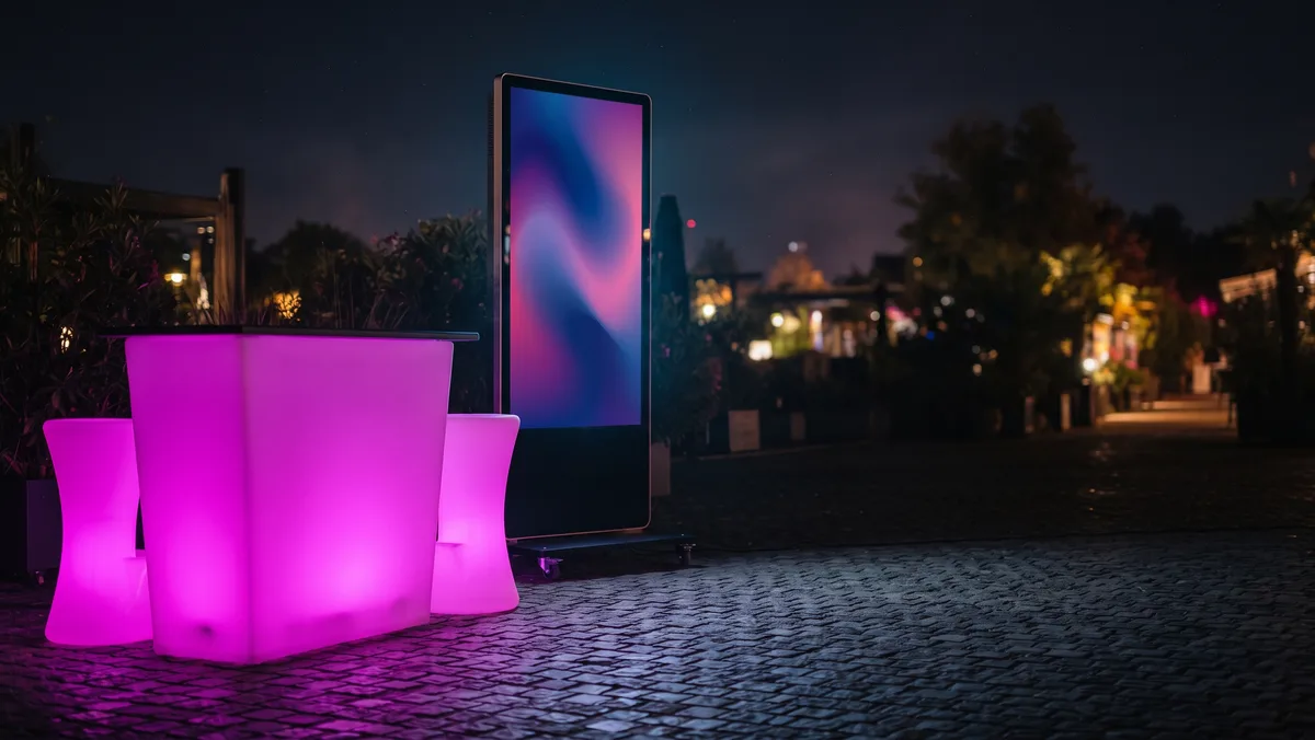 Világító LED bárpult és mögötte egy álló LED poszter panel egy kültéri rendezvény sarkában éjszaka
